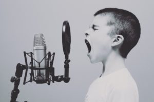 A young boy recording his voice using a microphone and pop filter.