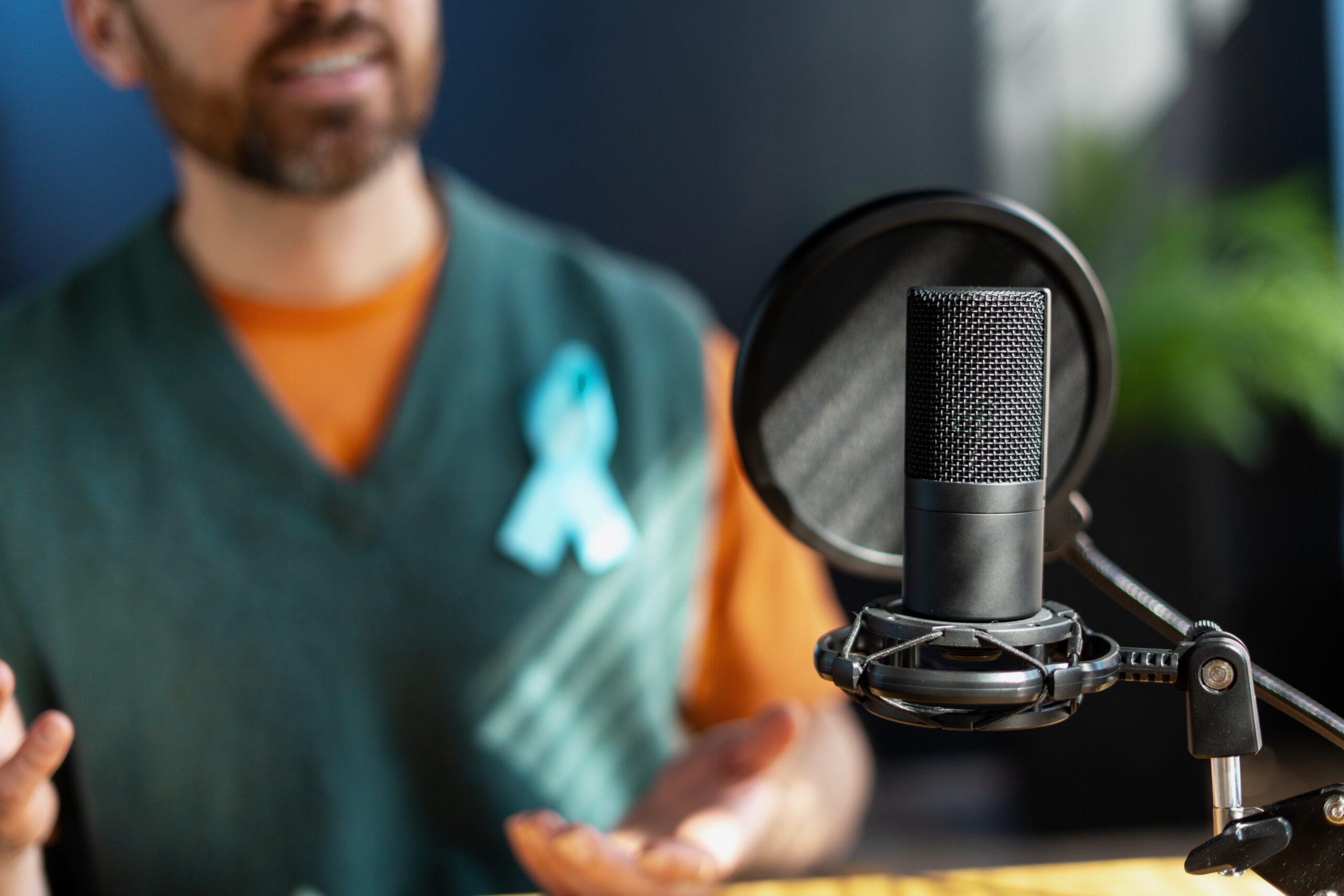 Podcaster wearing light blue awareness ribbon is recording audio content